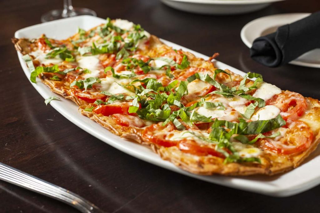 Close-up of Margherita flatbread garnished with torn basil.