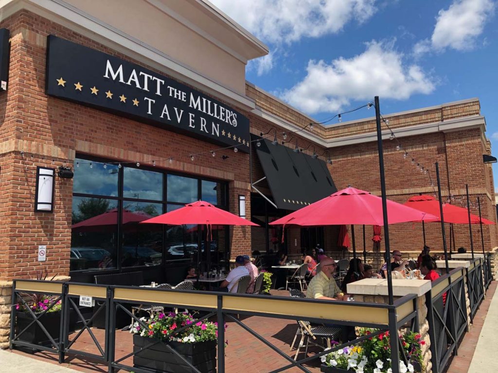 Outdoor patio with red umbrellas in front of Matt the Miller’s Tavern Gemini Place location.