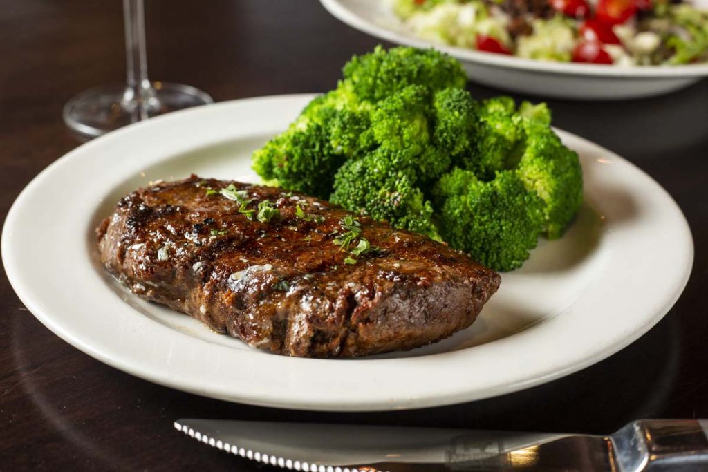 Sirloin steak plated with bright green broccoli and salad in background