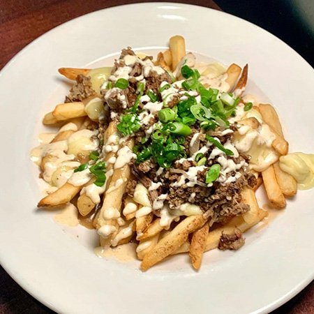 Plated Queen City poutine with thick Cut French Fries topped with Turkey Gravy, White Cheddar Cheese Curds, Glier’s Goetta, Pulled Pork, garlic crema and green onions