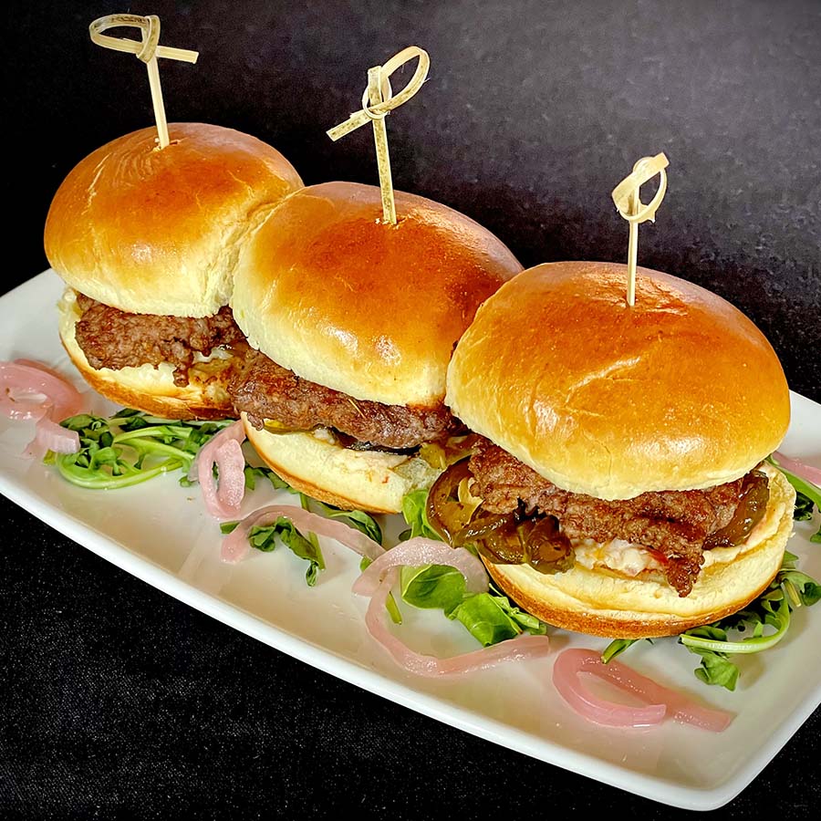 Three pimento cheeseburger sliders plated on rectangular plate.