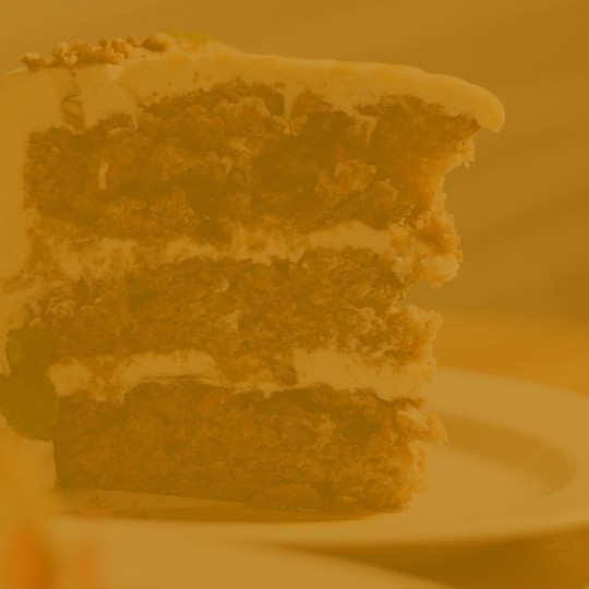 A tall slice of three-layer carrot cake with cream cheese frosting and chopped pecans on top