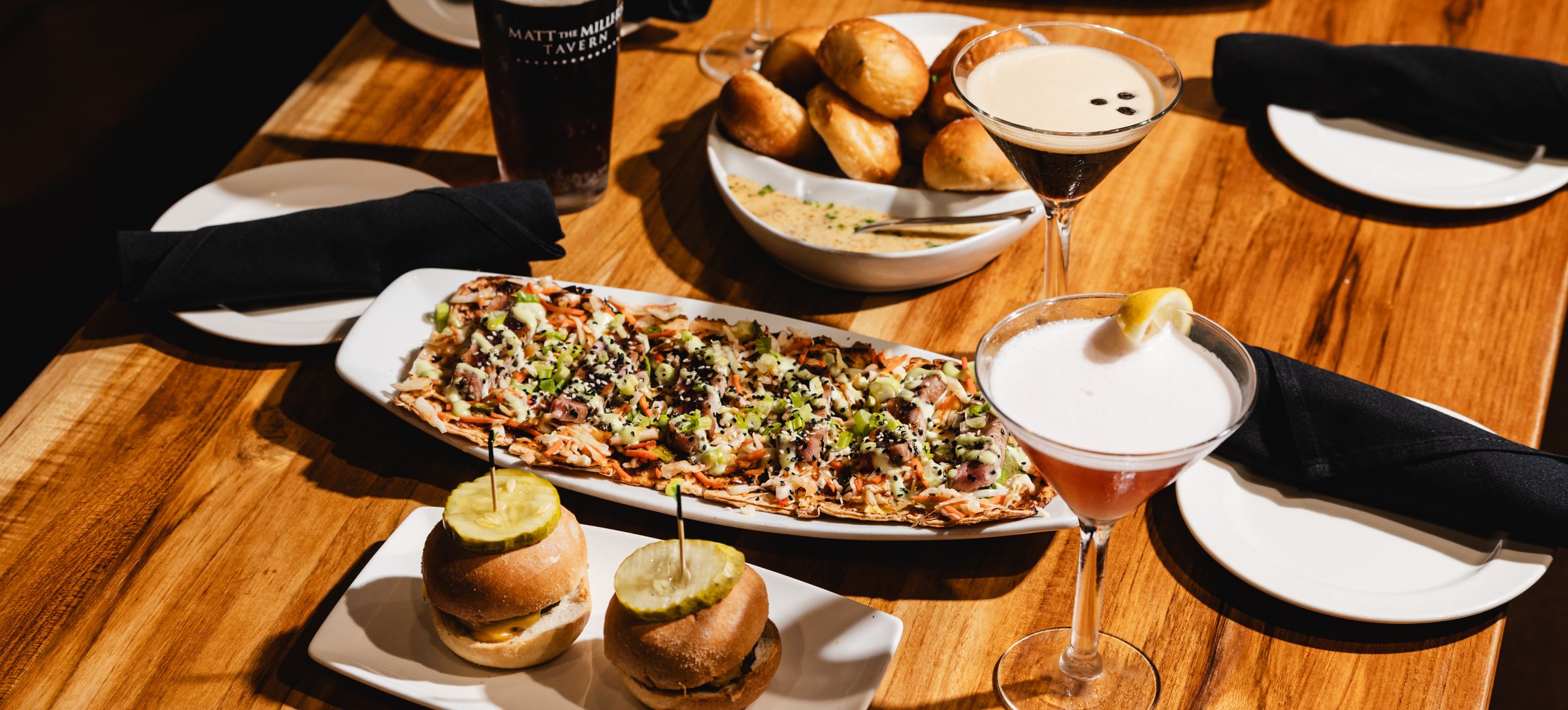Shared table of tuna flatbread, wagyu sliders, pretzel bites and cocktails