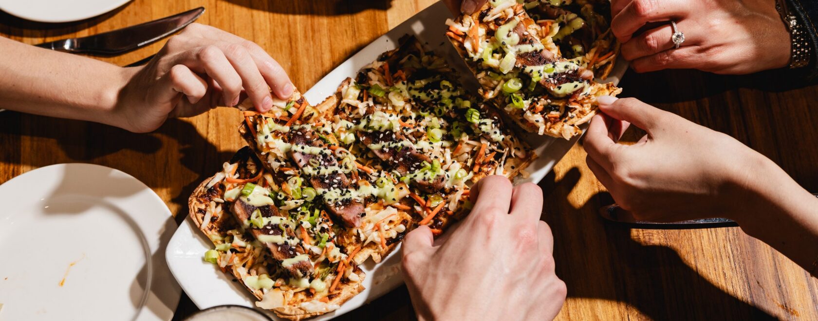 Friends reaching in to share the tuna flatbread